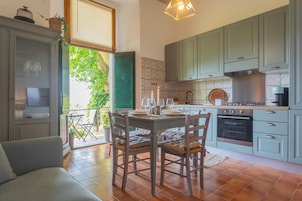 Una cocina con armarios verde claro, una mesa de comedor para cuatro personas y un ventanal con vistas a la vegetación.