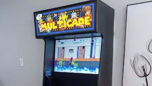 Une borne d’arcade de jeux vidéo, avec un panneau néon, un panneau de contrôle et un tableau encadré accroché au mur.
