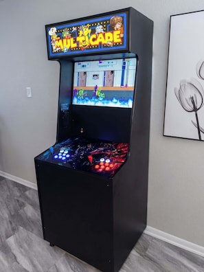 A video game arcade machine with a neon sign, a control panel, and a framed picture on the wall.
