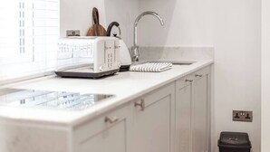 A kitchen with a white countertop, a toaster, a kettle, a sink, and a window with blinds. - Spacious Stylish Studio, Hoylake (Hoylake)