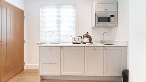 A kitchen with white cabinets, a microwave, a toaster, and a kettle. - Spacious Stylish Studio, Hoylake (Hoylake)