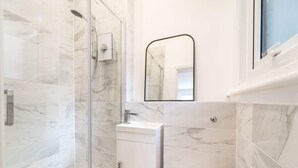 A bathroom with a glass shower enclosure, a white sink, and a mirror above the sink. - Spacious Stylish Studio, Hoylake (Hoylake)