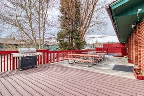 Enjoy al fresco dining and relaxation on the patio, featuring a barbecue grill, picnic tables, and a brick wall surrounded by a fence and a large tree.