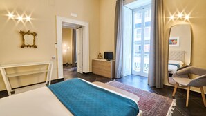 Ein Hotelzimmer mit einem Bett, einem Schreibtisch, einem Stuhl, einer Kommode und einem großen Fenster mit Vorhängen.