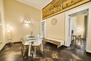 A dining area with a glass table and chairs, a wall clock, and a large painting above the door. - Via Niccol Tommaseo 14 (Naples)
