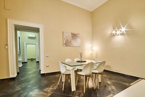 A dining area with a glass table, white chairs, a wall-mounted light, and a door leading to another room. - Via Niccol Tommaseo 14 (Naples)