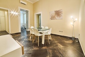 A dining area with a glass table and white chairs, a kitchen with white cabinets, and a hallway leading to another room. - Via Niccol Tommaseo 14 (Naples)