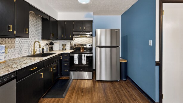 A modern kitchen with black cabinets, stainless steel appliances, and a blue accent wall.