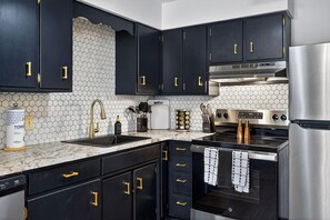 Eine moderne Küche mit schwarzen Schränken, einem Edelstahlkühlschrank, einem eingebauten Backofen und einer Mikrowelle.