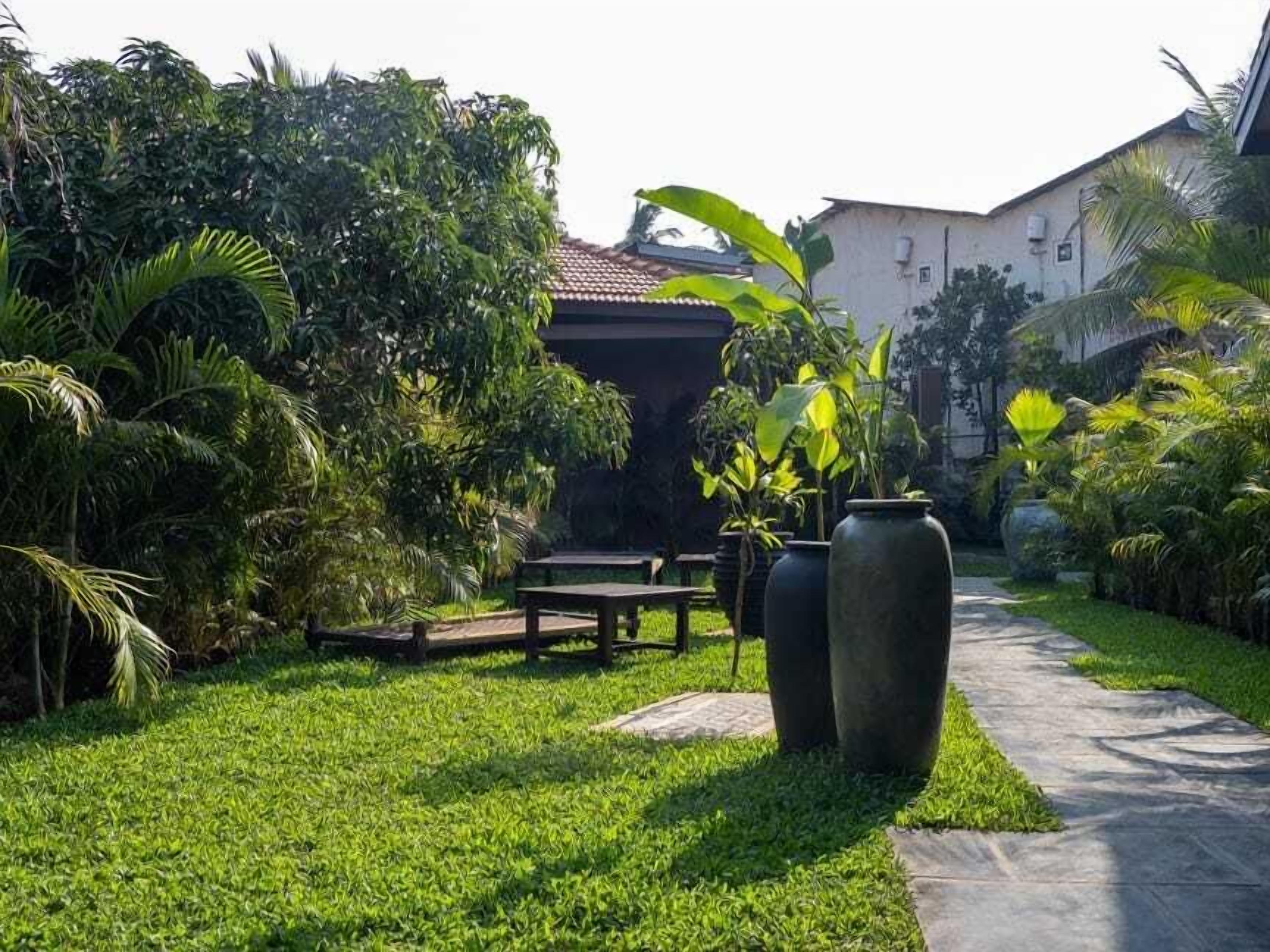 Un jardín bien cuidado con un sendero, una mesa de madera y jarrones grandes.
