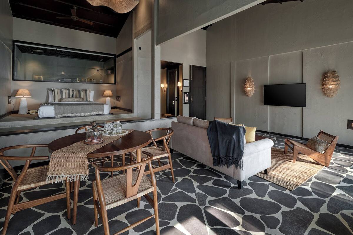 Una sala de estar moderna con suelo estampado en piedra, un sofá, un televisor y una zona de comedor con sillas de mimbre y una mesa de madera.