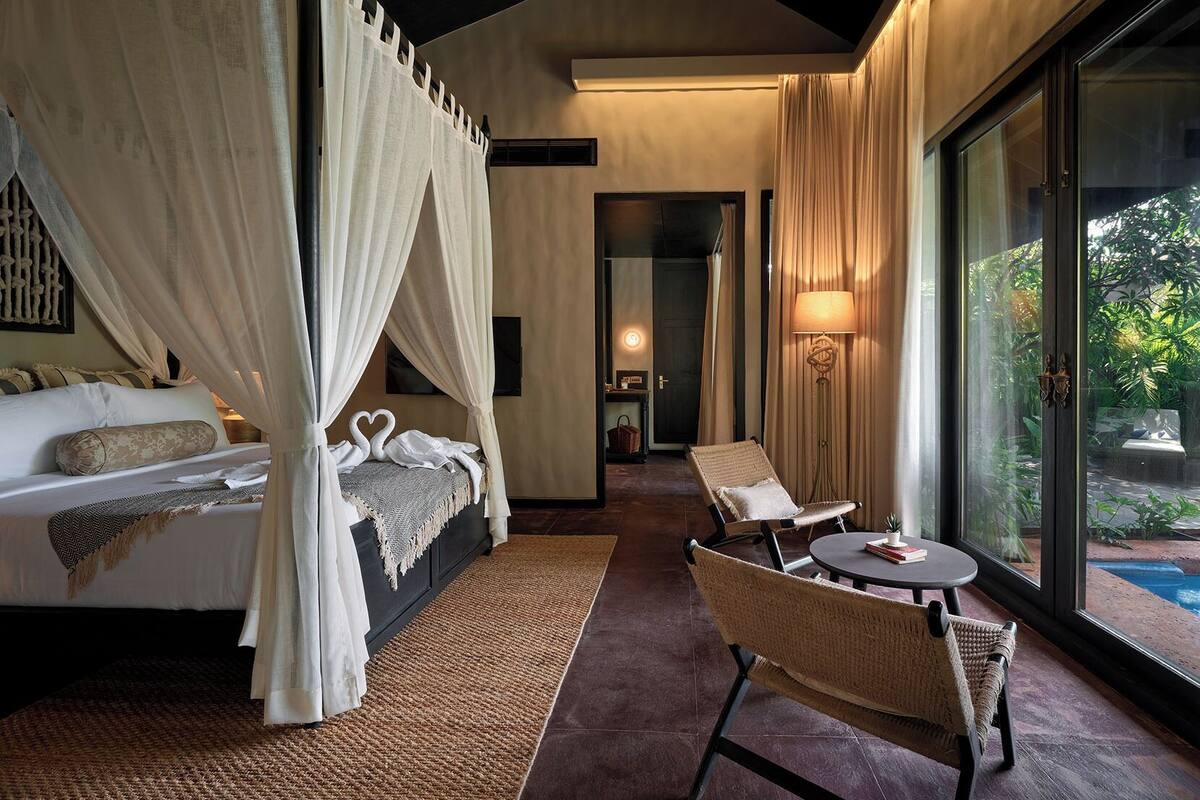Un dormitorio con cama con dosel, una zona de estar con mesa y sillas, y vistas a una piscina.