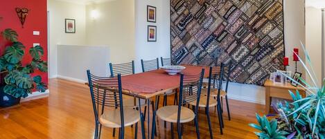 A dining area with a wooden table and chairs, a red wall, and a patterned tapestry.