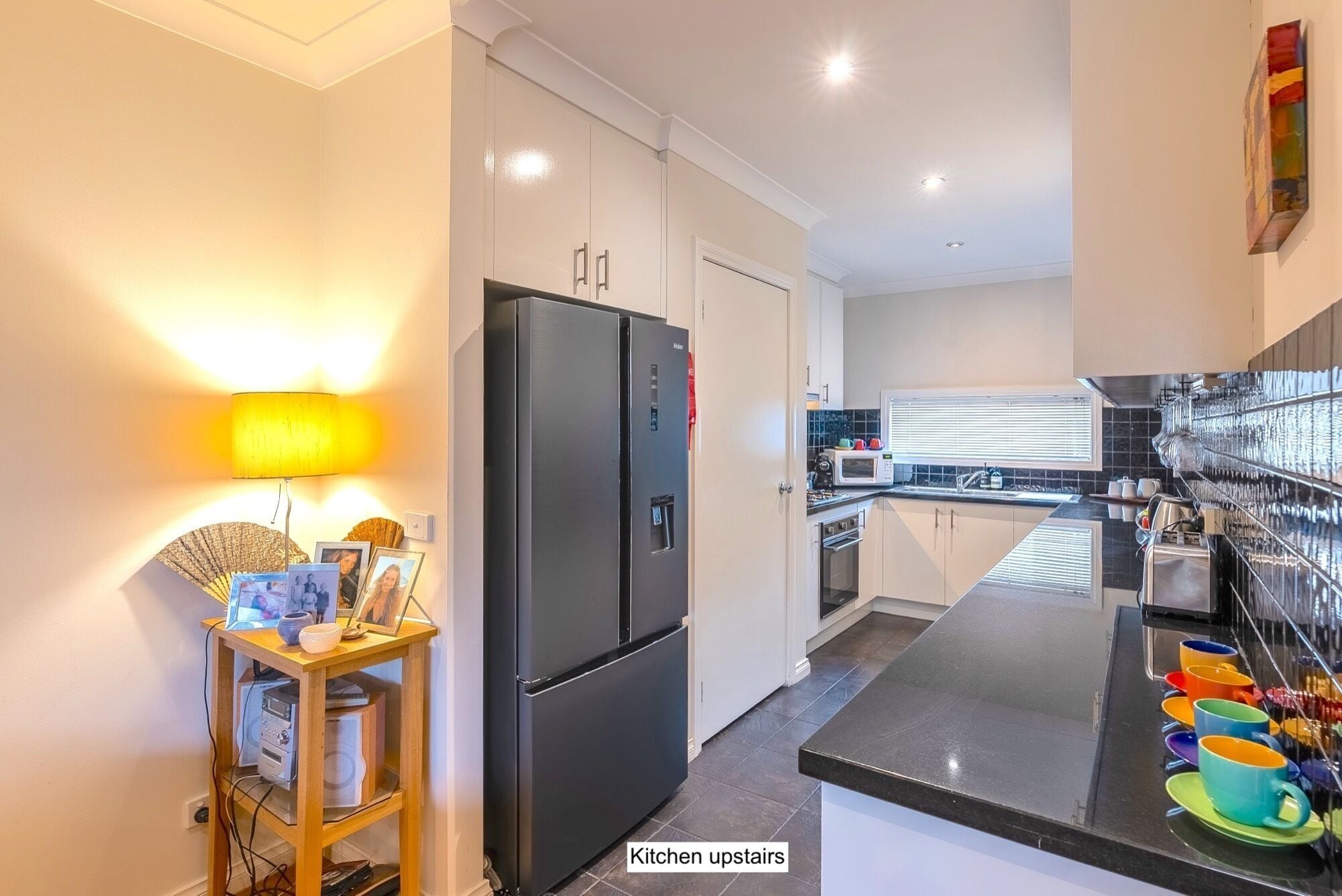 Une cuisine moderne avec un réfrigérateur noir, un buffet en bois et une petite table avec une lampe.