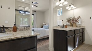 A modern bathroom with a large mirror, dark cabinetry, and a granite countertop.