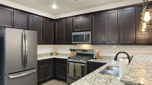 A modern kitchen with dark wood cabinets, stainless steel appliances, granite countertops, and a built-in microwave.
