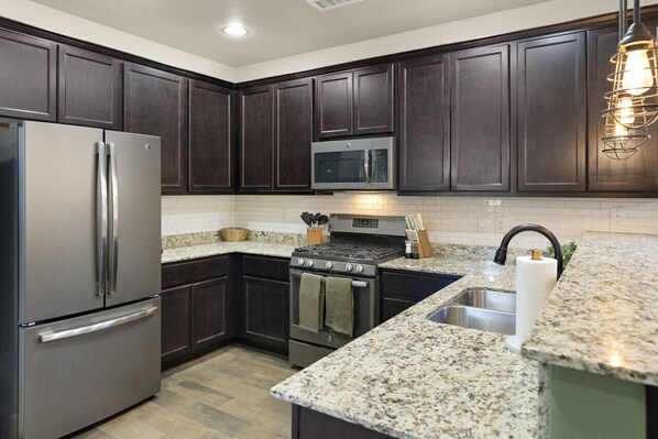 A modern kitchen with dark wood cabinets, stainless steel appliances, granite countertops, and a built-in microwave.