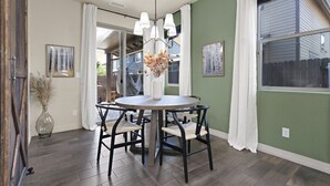 A dining area with a round table, black chairs, a vase with dried flowers, and a chandelier.
