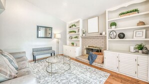Een woonkamer met een bank, een rond bijzettafeltje, een open haard en witte planken met decoratieve objecten.