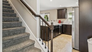 A staircase leading to a kitchen with dark wooden cabinets and a stainless steel refrigerator. - New 3BR Townhome | Small Dogs OK | Near Public Boat Ramp | Green Cove Springs (Green Cove Springs)
