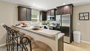 A modern kitchen with dark wood cabinets, stainless steel appliances, and a central island with bar stools. - New 3BR Townhome | Small Dogs OK | Near Public Boat Ramp | Green Cove Springs (Green Cove Springs)
