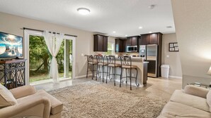 A modern kitchen with dark cabinets, a stainless steel refrigerator, and a microwave. There is a bar area with stools and a large window overlooking a garden. - New 3BR Townhome | Small Dogs OK | Near Public Boat Ramp | Green Cove Springs (Green Cove Springs)