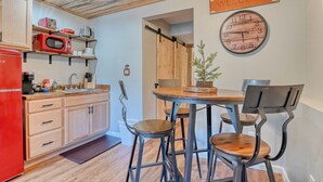 Una cocina compacta con armarios de madera, un refrigerador rojo y una zona de comedor con una mesa de madera y sillas de metal.