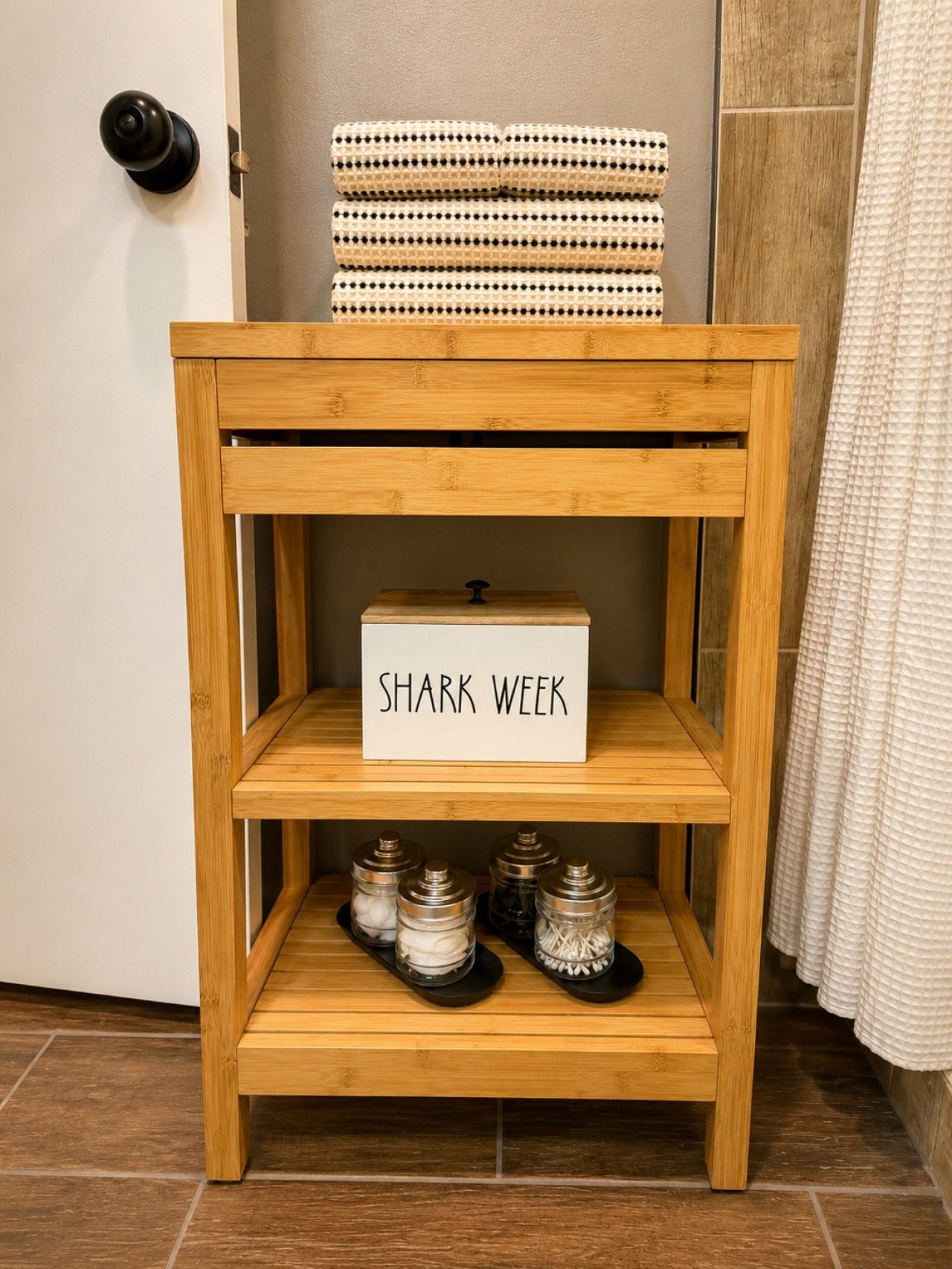 A wooden side table with a sign that reads 'SHARK WEEK' and three shelves below containing jars.