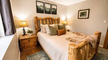 Un dormitorio con cabecera de madera, una cama con varias almohadas, una mesita de noche con una lámpara y una planta pequeña.