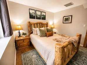Un dormitorio con cabecera de madera, una cama con varias almohadas, una mesita de noche con una lámpara y una planta pequeña.