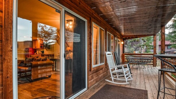 Una cabaña de madera con porche cubierto, puertas de vidrio correderas y un espacio de estar con mecedora y mesa.