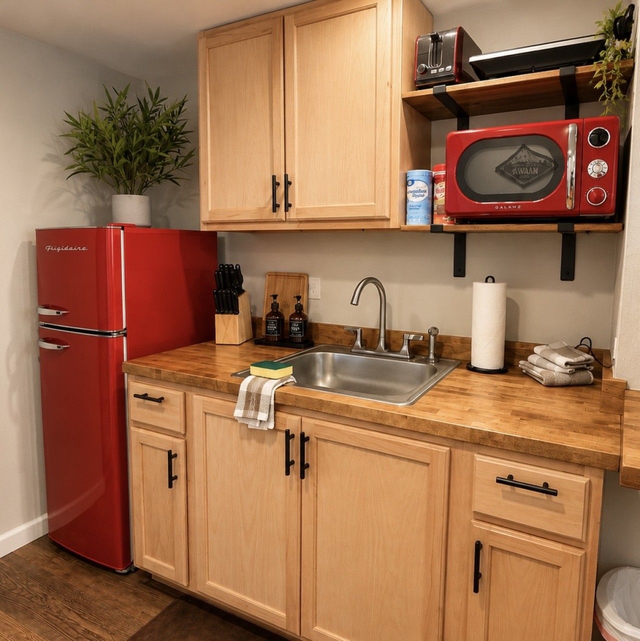 Une cuisine compacte avec des meubles en bois, un réfrigérateur rouge, un évier en acier inoxydable et un four à micro-ondes rouge.