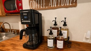 Una cocina con cafetera, microondas y botellas etiquetadas de sirope para café.