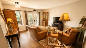 Una sala de estar acogedora con un sofá, un sillón y una mesa de centro. Hay un televisor, una lámpara y un aparador de madera.
