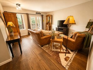 A cozy living room with a sofa, armchair, and a coffee table. There is a television, a lamp, and a wooden cabinet. - Beaver Lodge Near Pikes Peak & Manitou Springc GMF (Green Mountain Falls)