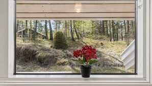 A window with a view of a forested area, a small potted plant with red flowers, and a white structure in the background. - "Sylvia" - 900m from the sea by Interhome (Nexø)