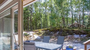 A deck with a table and chairs overlooking a forested area with a cabin in the background. - "Sylvia" - 900m from the sea by Interhome (Nexø)