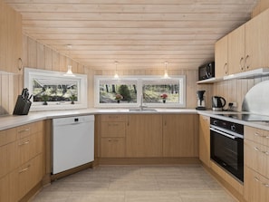 Eine moderne Küche mit Holzschränken, einem Geschirrspüler, einem Herd und einer Kaffeemaschine.