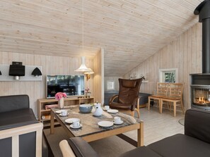 Ein gemütliches Zimmer mit Kamin, Holzwänden, Fernseher und Essecke mit Tisch für zwei Personen.