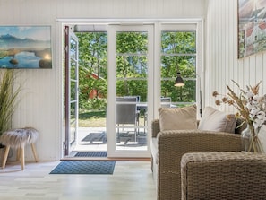 A room with a wicker sofa, a dining table, and a large sliding glass door leading to an outdoor area with a view of trees and a building.