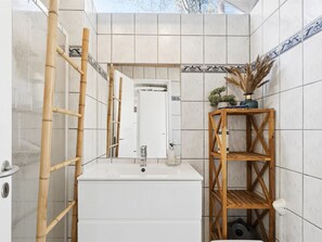 A bathroom with a white sink, bamboo ladder, a wooden shelf with plants, and a tiled wall with decorative borders.