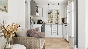 A compact kitchen with white cabinets, a refrigerator, and a dining area with wicker furniture. - "Blakke" - 250m from the sea by Interhome (Nexø)