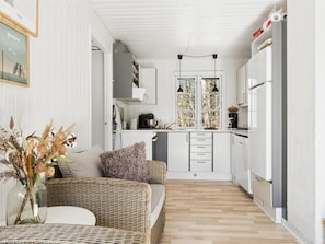 A compact kitchen with white cabinets, a refrigerator, and a dining area with wicker furniture.