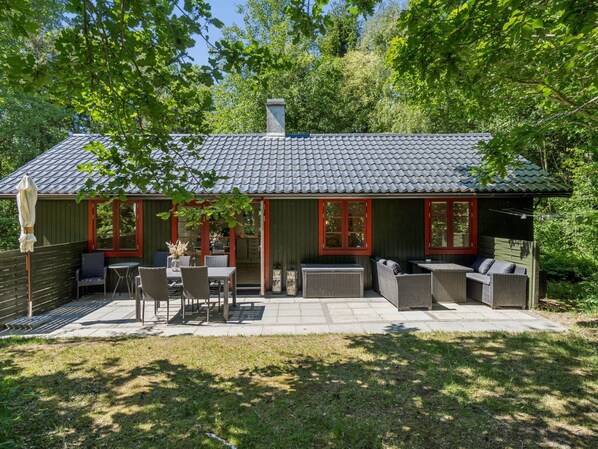 A wooden cabin with a tiled roof, outdoor seating area, and a covered patio.