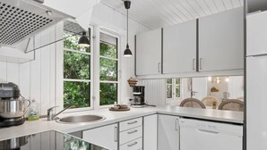 A modern kitchen with white cabinetry, a black induction cooktop, a built-in dishwasher, and a window providing a view of greenery. - "Blakke" - 250m from the sea by Interhome (Nexø)