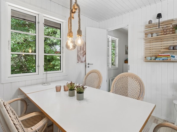 A dining area with a white table, wicker chairs, and a hanging light fixture.