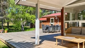 Een overdekt terras met een houten dek, een bank en een tafel.