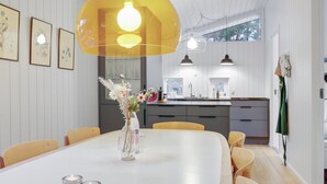 Een moderne eethoek met een witte tafel, gele stoelen en een grote gele hanglamp.