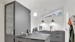 Een moderne keuken met grijze kastjes, een centraal eiland, hanglampen en uitzicht op de omgeving.