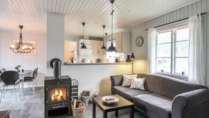 Ein gemütliches Wohnzimmer mit Kamin, einer Couch, einem Essbereich mit Stühlen und einer Küche im Hintergrund.